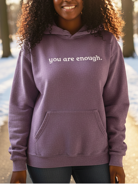 Person wearing a purple hoodie with 'you are enough' text in a snowy forest setting